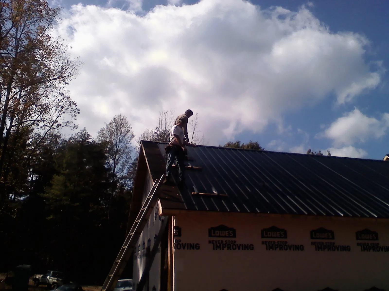 Roofer fastening dark metal panels high against a cloudy sky, from a Roof Inspection job in Hoboken