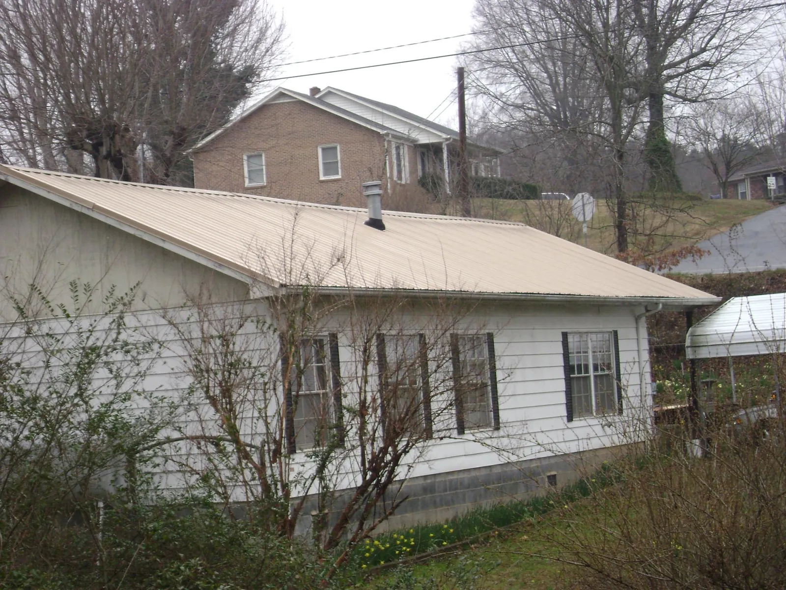 Tan metal roof on a white sided house set into a hillside — Commercial Roofing by Roofing Brothers in Hoboken